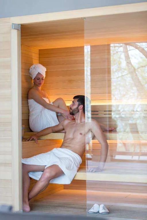 Sauna in legno con coppia rilassata e ampia vetrata sul giardino