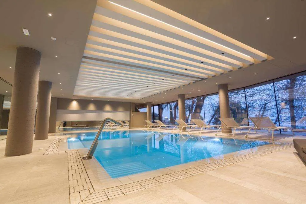 Piscina interna riscaldata con lettini e ampie vetrate sul parco