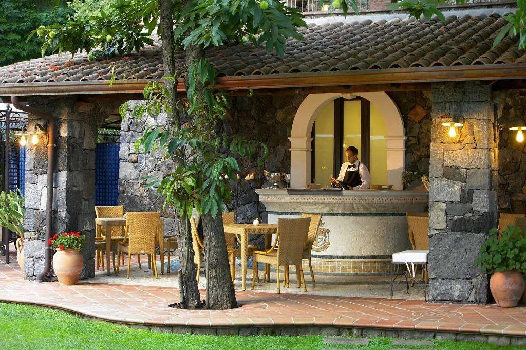 Bar esterno in pietra con tavoli, sedie in vimini e barista