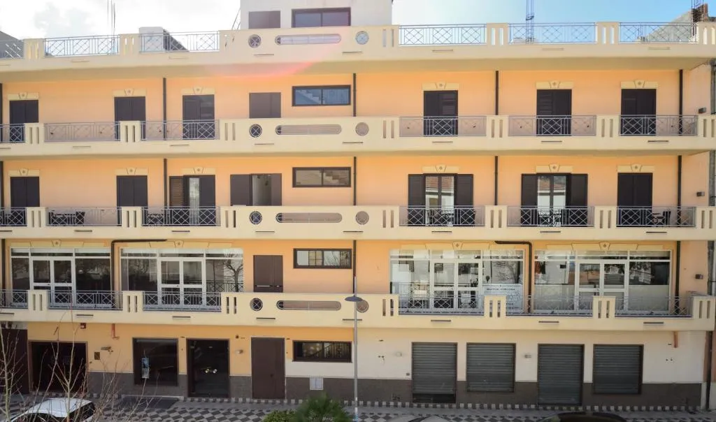 Facciata esterna di edificio color pesca con balconi in ferro battuto e persiane