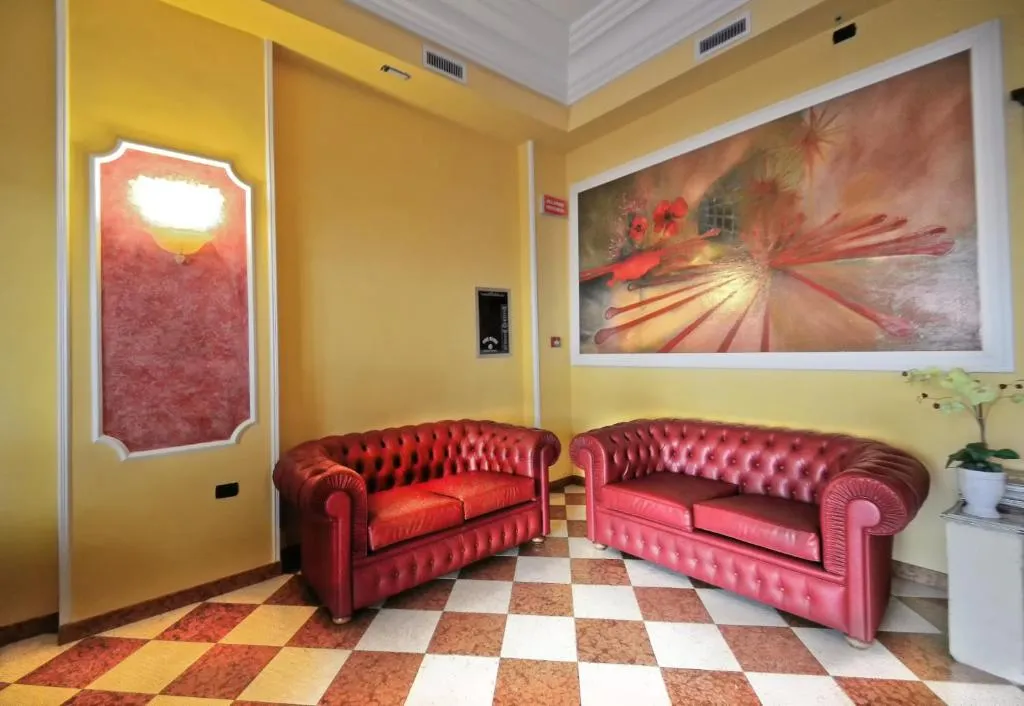 Hall con due divani Chesterfield in pelle rossa, pavimento a scacchi e grande quadro alle pareti
