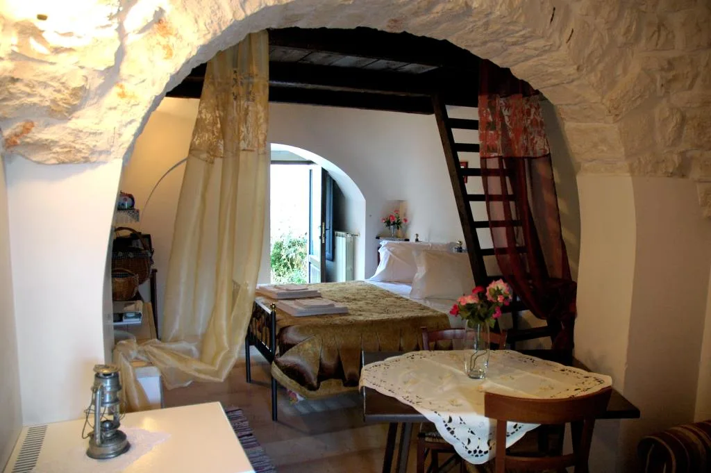 Camera in trullo con arco in pietra, letto matrimoniale e scala per soppalco