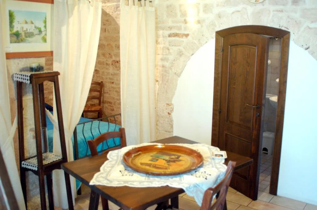 Zona pranzo in trullo con tavolo in legno, letto e porta del bagno