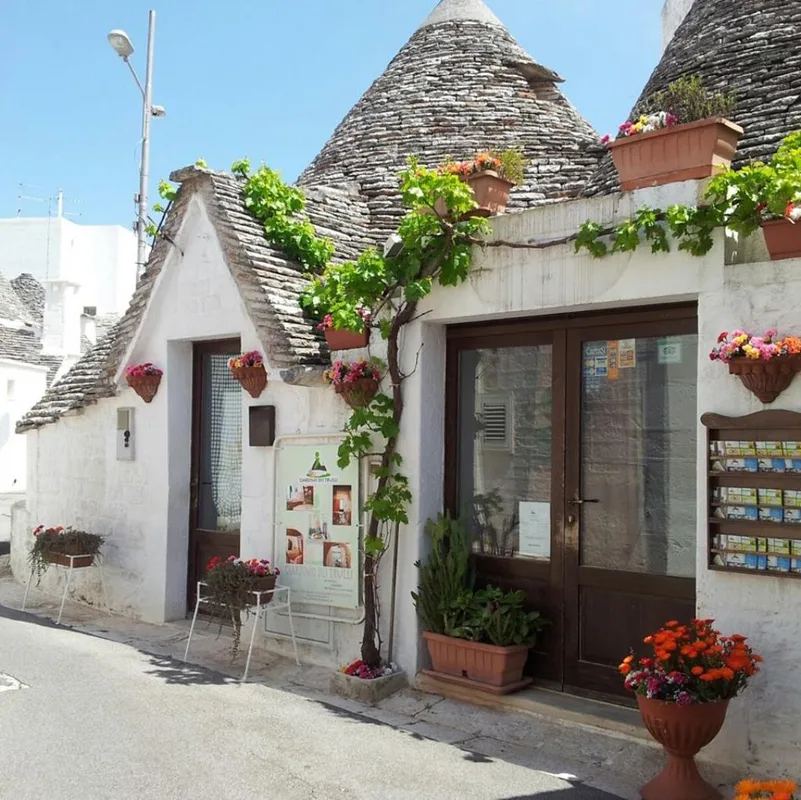 Facciata esterna di trullo con fiori colorati in vaso e tetti conici in pietra