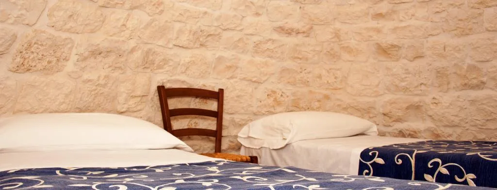 Dettaglio di due letti con parete in pietra e copriletto blu decorato