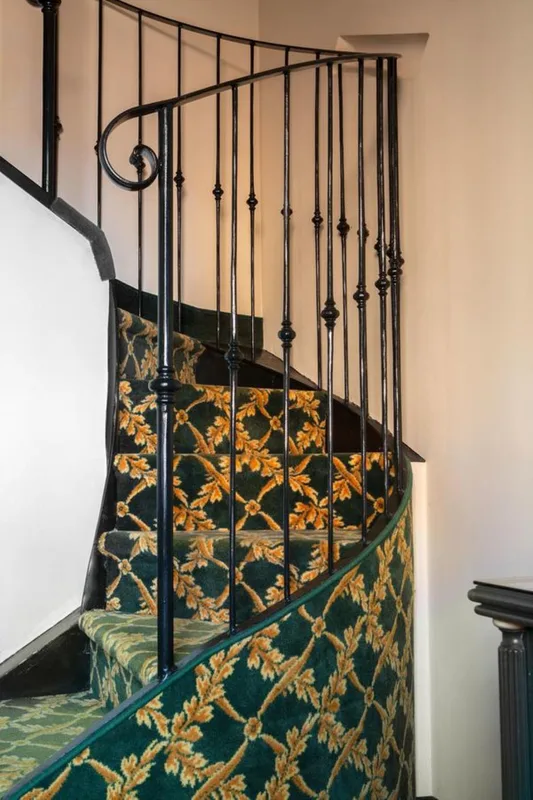 Scala a chiocciola con ringhiera in ferro battuto e tappeto verde a motivi floreali dorati