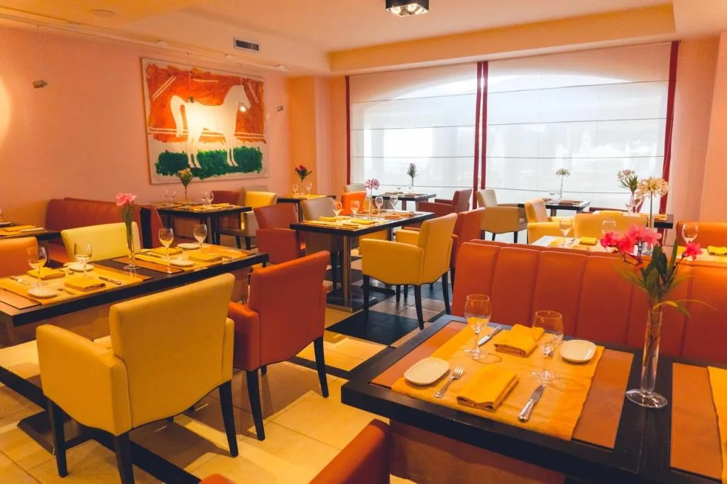 Sala ristorante con tavoli apparecchiati, sedie gialle e arancioni e ampie finestre