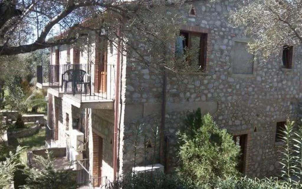 Edificio in pietra a più piani con balcone, immerso tra ulivi e vegetazione
