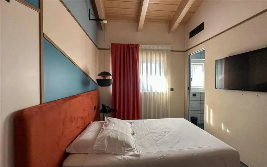Camera con soffitto in legno, letto matrimoniale, TV a parete e tenda rossa