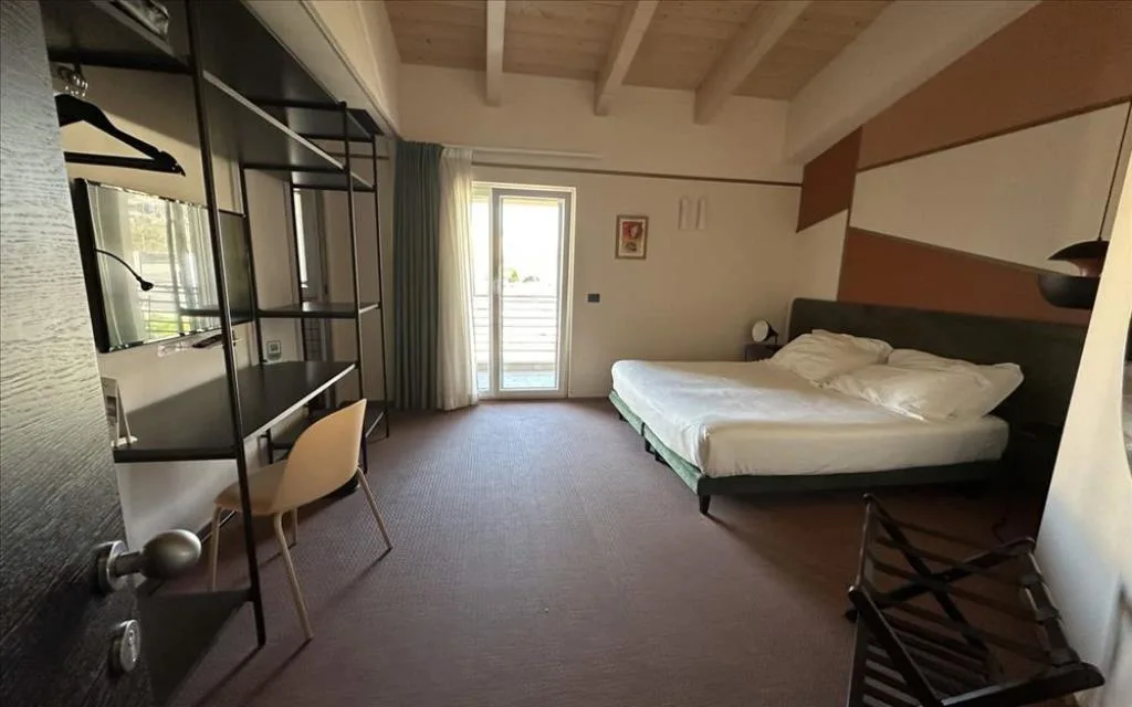 Ampia camera con soffitto in legno, letto matrimoniale, scrivania e porta finestra sul balcone