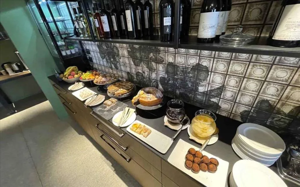 Buffet dolce con torte, biscotti, frutta e bottiglie di vino su parete piastrellata