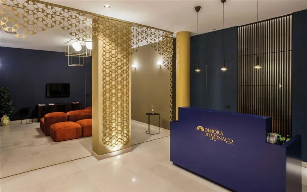 Reception dell'hotel con bancone blu, colonna decorata a nido d'ape e area salotto