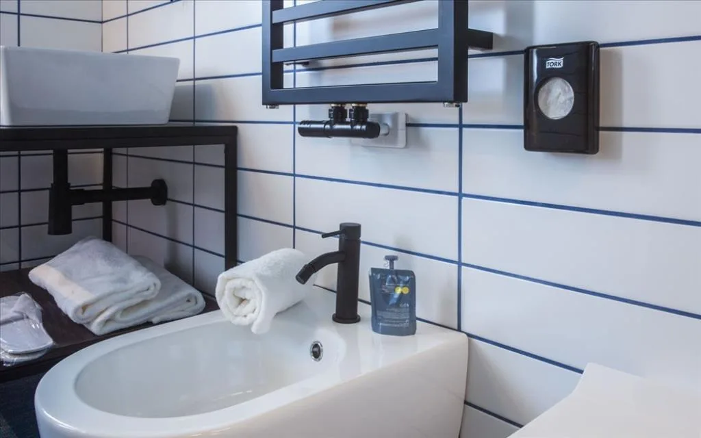 Dettaglio del lavabo con rubinetteria nera, asciugamani e sapone su piastrelle bianche