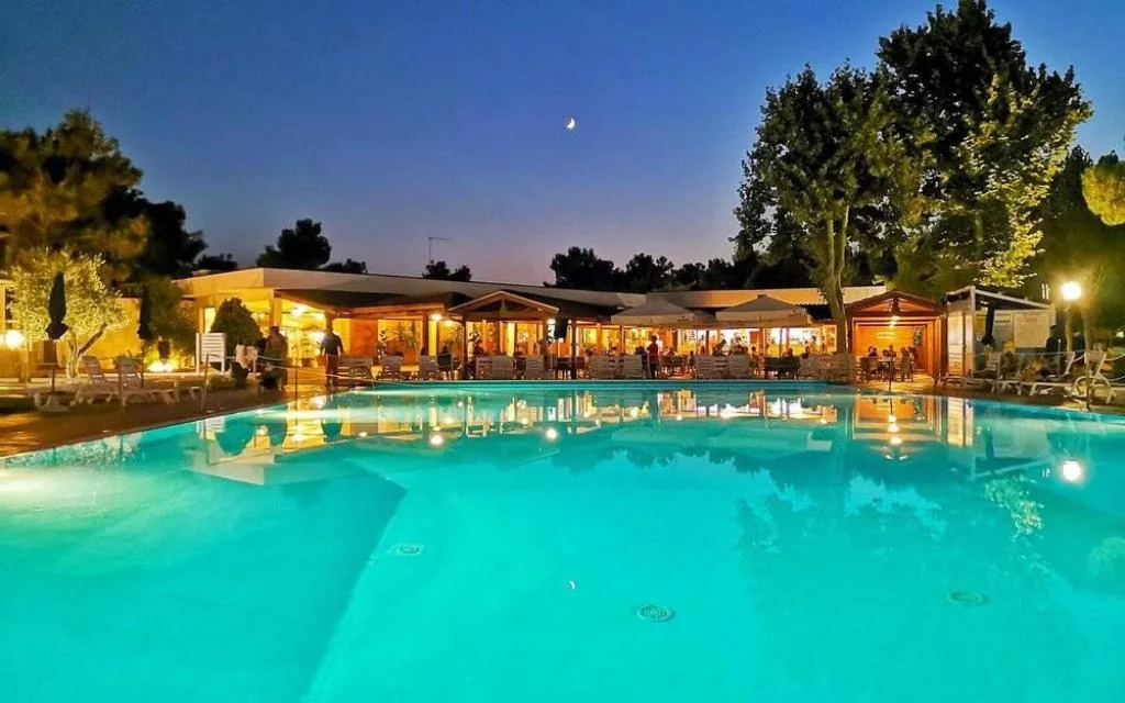 Piscina illuminata al tramonto con ristorante e area lounge sullo sfondo