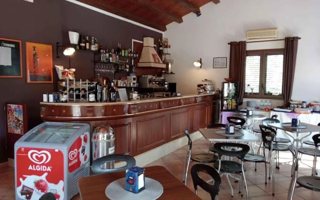 Bar interno con bancone in legno, tavolini e frigo gelati