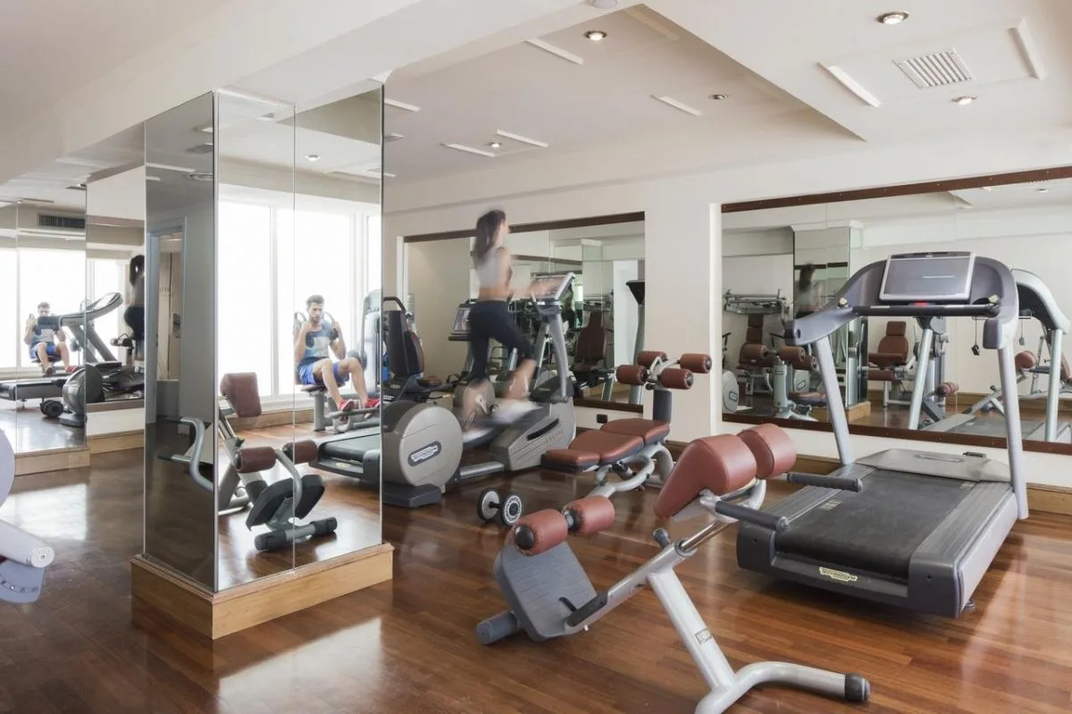 Palestra attrezzata con tapis roulant e macchine cardio, pavimento in legno e pareti a specchio