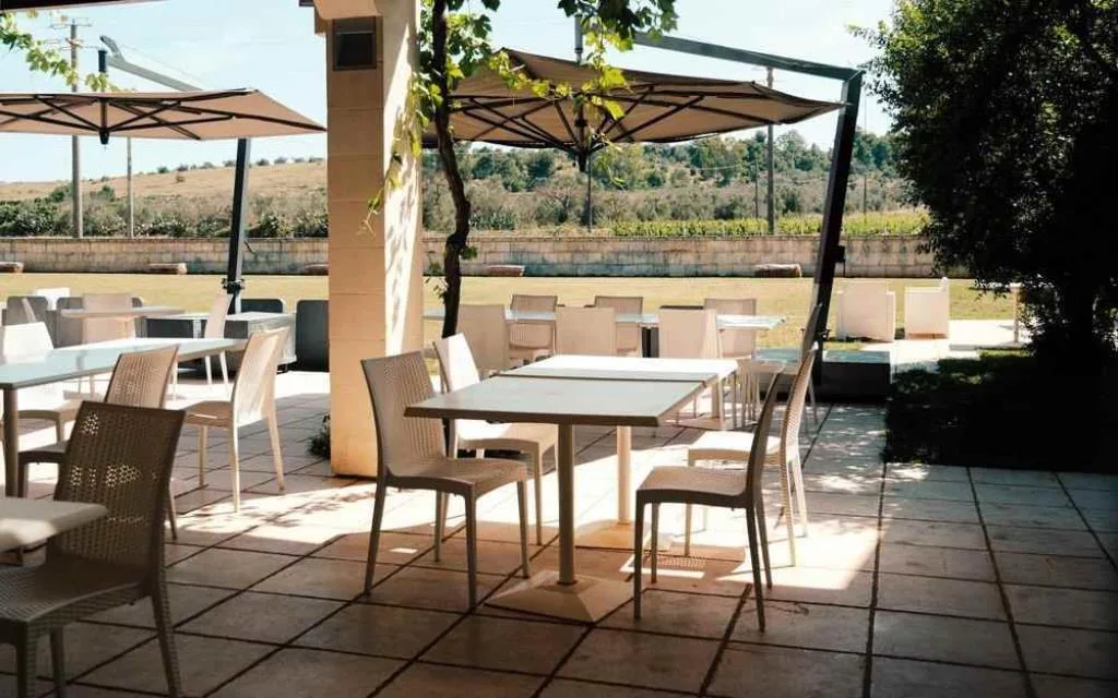 Terrazza esterna del ristorante con tavoli bianchi e ombrelloni, vista sui campi