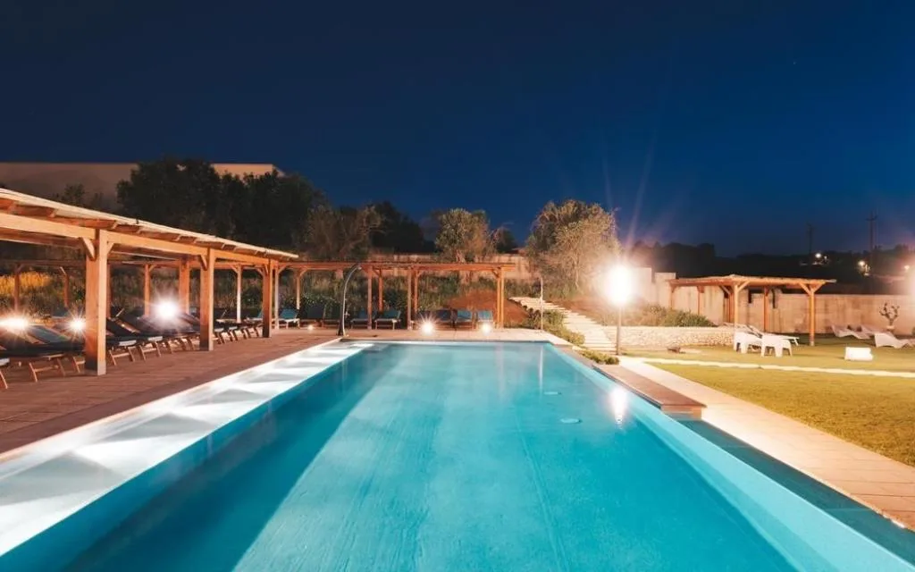 Piscina illuminata di sera con pergolati in legno e luci soffuse