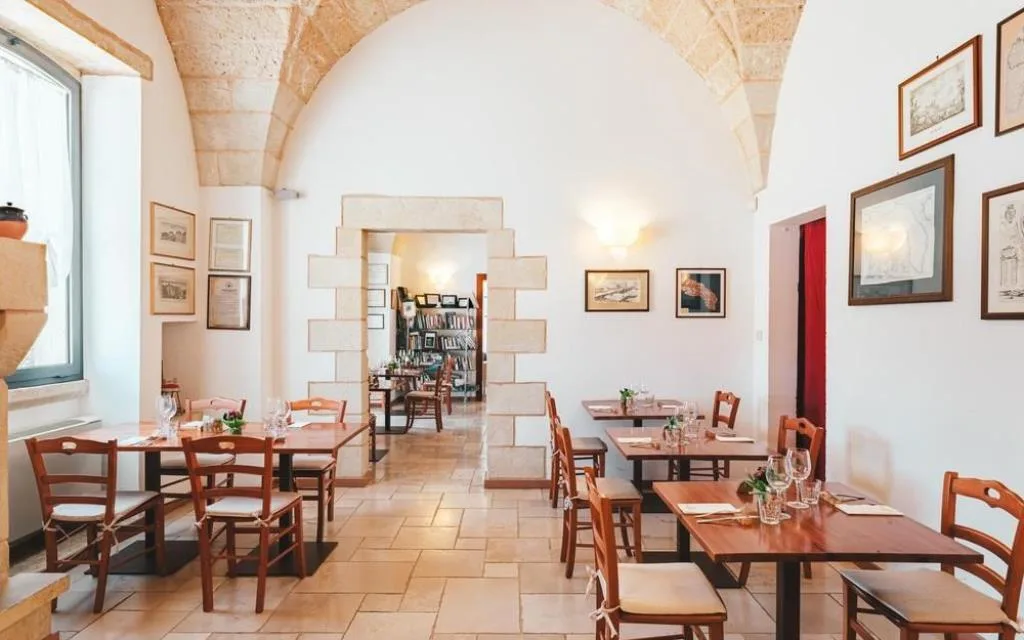 Sala ristorante con soffitto a volta in pietra, tavoli apparecchiati e quadri alle pareti
