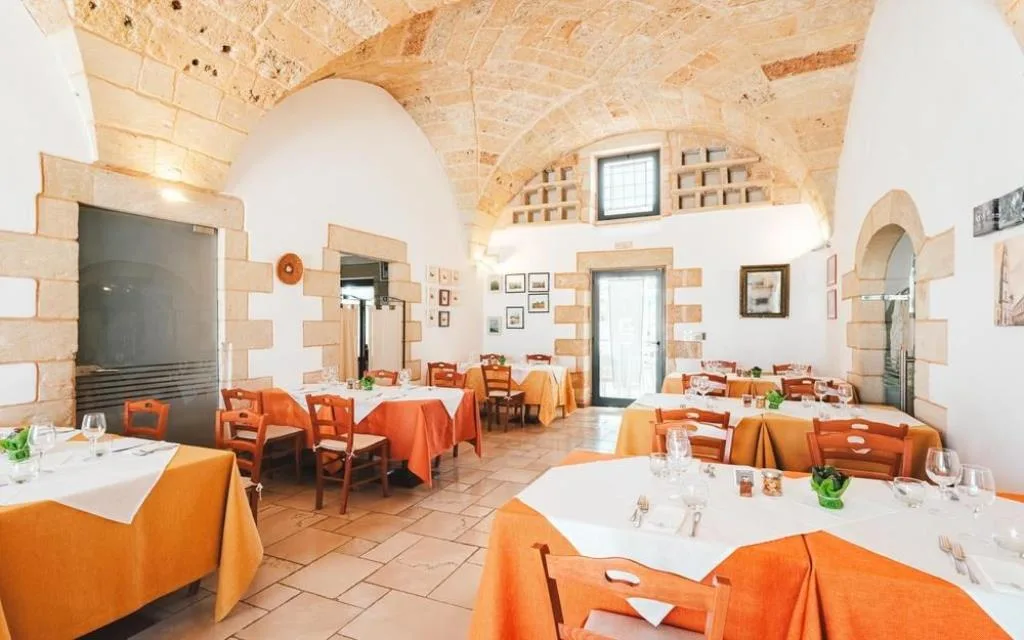 Sala ristorante con volte in pietra e tovaglie arancioni apparecchiate