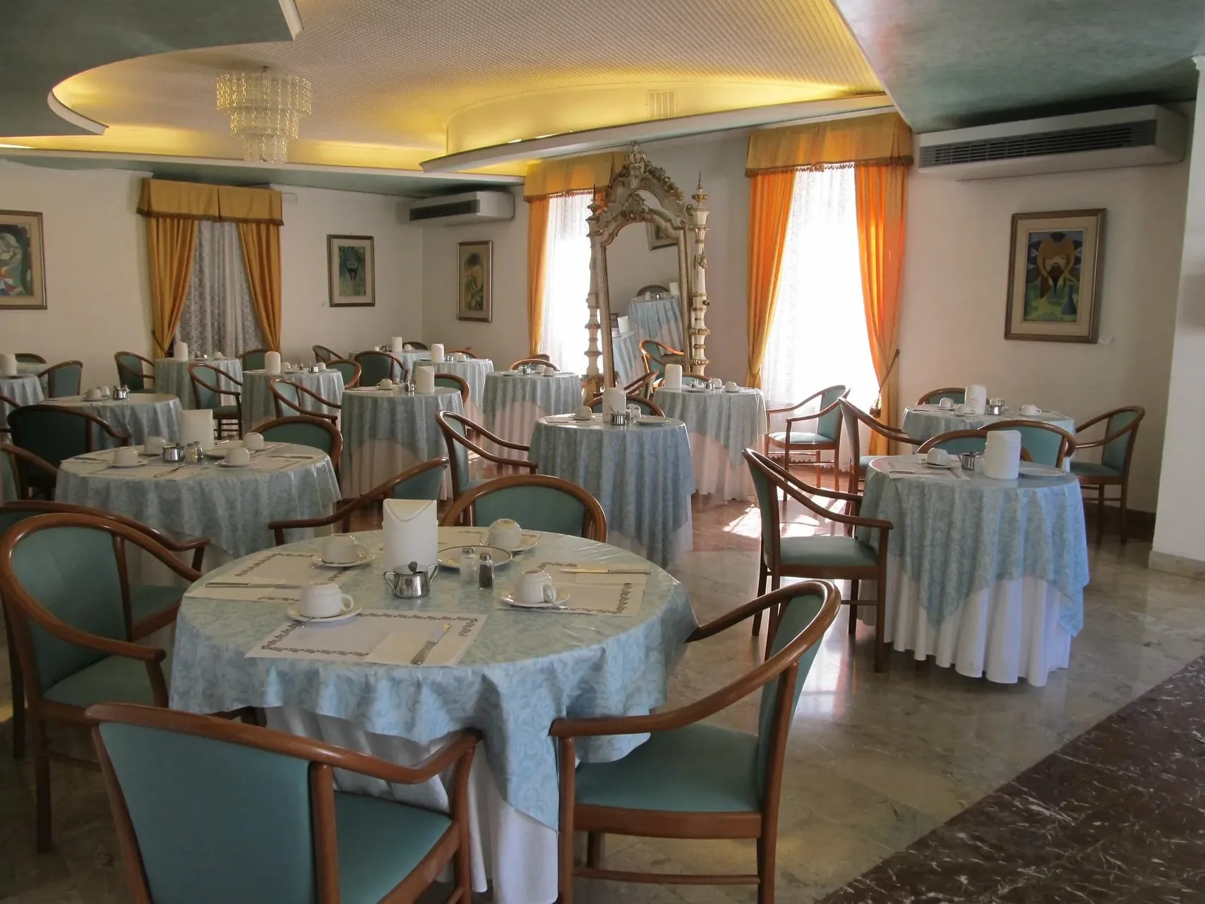 Sala colazione con tavoli rotondi apparecchiati, tovaglie azzurre e specchio decorato