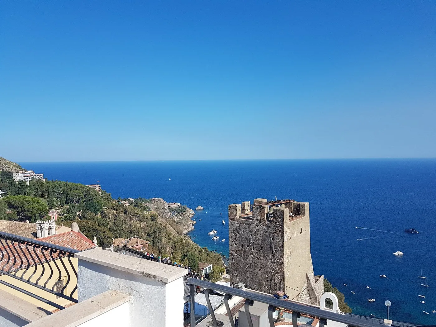Vista panoramica dal balcone sul mare turchese, torre storica e barche