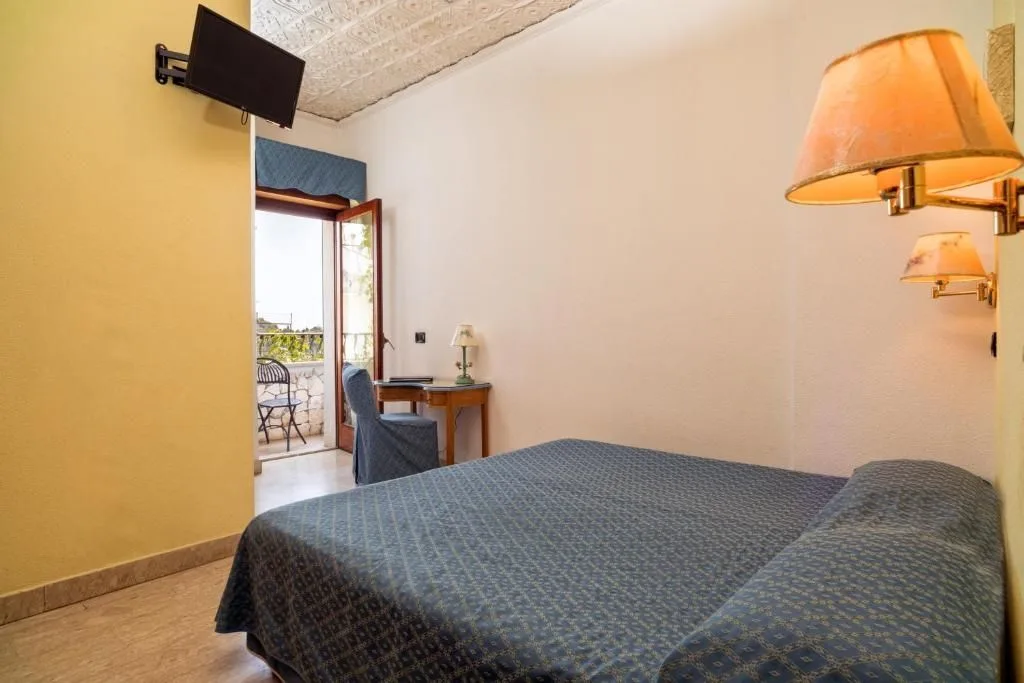 Camera con letto matrimoniale blu, TV a parete e porta finestra sul balcone