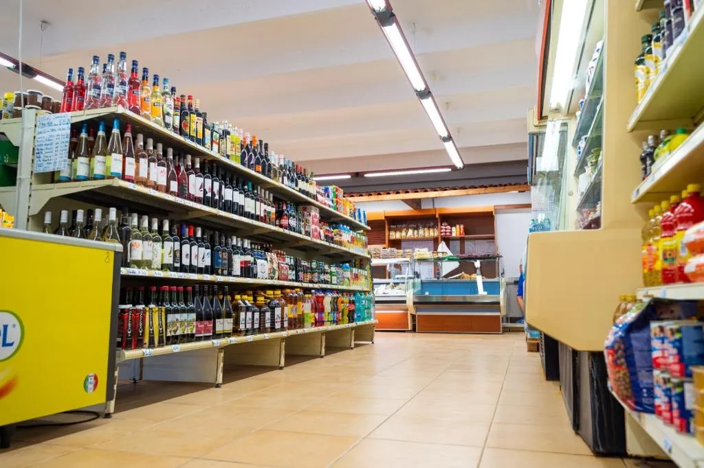 Interno del minimarket con scaffali di bevande, prodotti alimentari e banco gastronomia