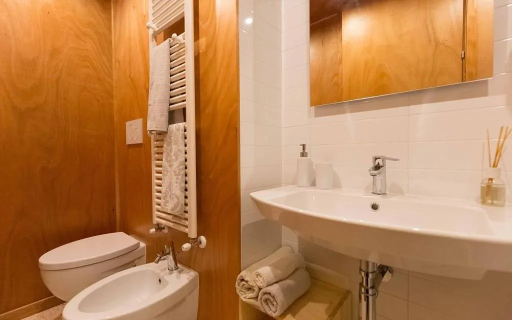 Bagno con lavabo, sanitari bianchi, bidet e scaldasalviette con pareti in legno