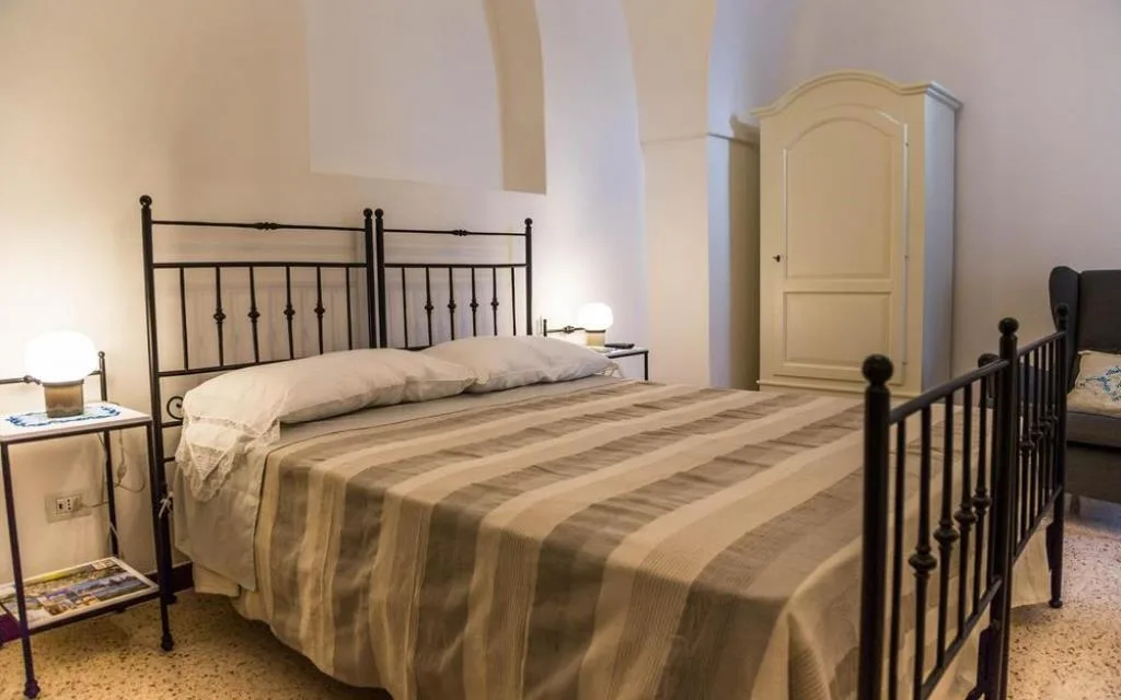 Camera da letto matrimoniale con testiera in ferro battuto nero, copriletto a righe e armadio bianco