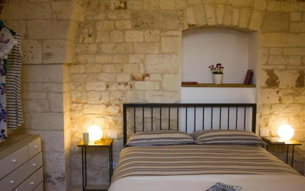 Camera con letto in ferro battuto, pareti in pietra a vista, nicchia con piante e comodini illuminati