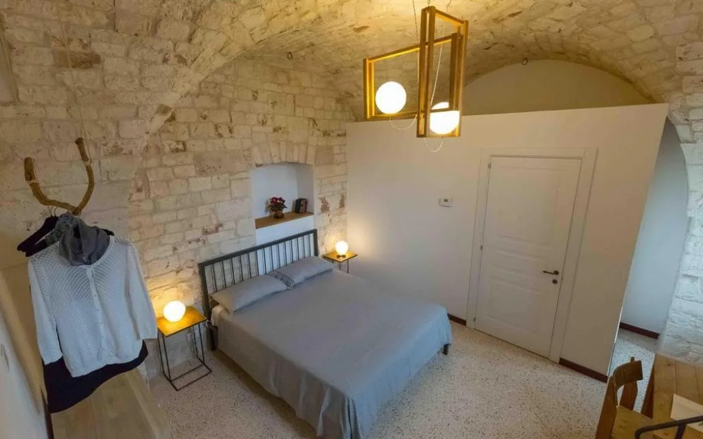 Camera con soffitto a volta in pietra, letto matrimoniale, lampada di design dorata e nicchia decorativa
