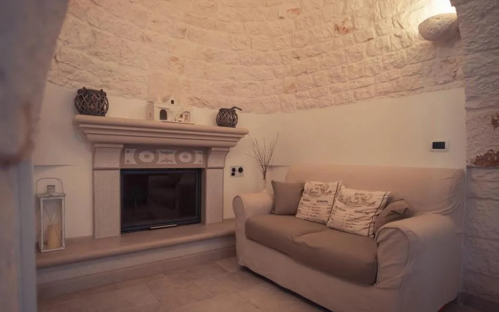 Salotto in trullo con camino in pietra, divano beige e cuscini decorativi