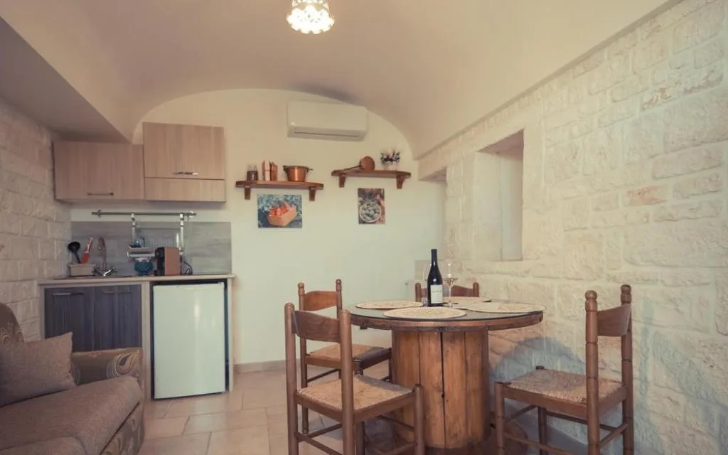 Angolo cottura in trullo con tavolo in legno, sedie impagliate e cucina compatta