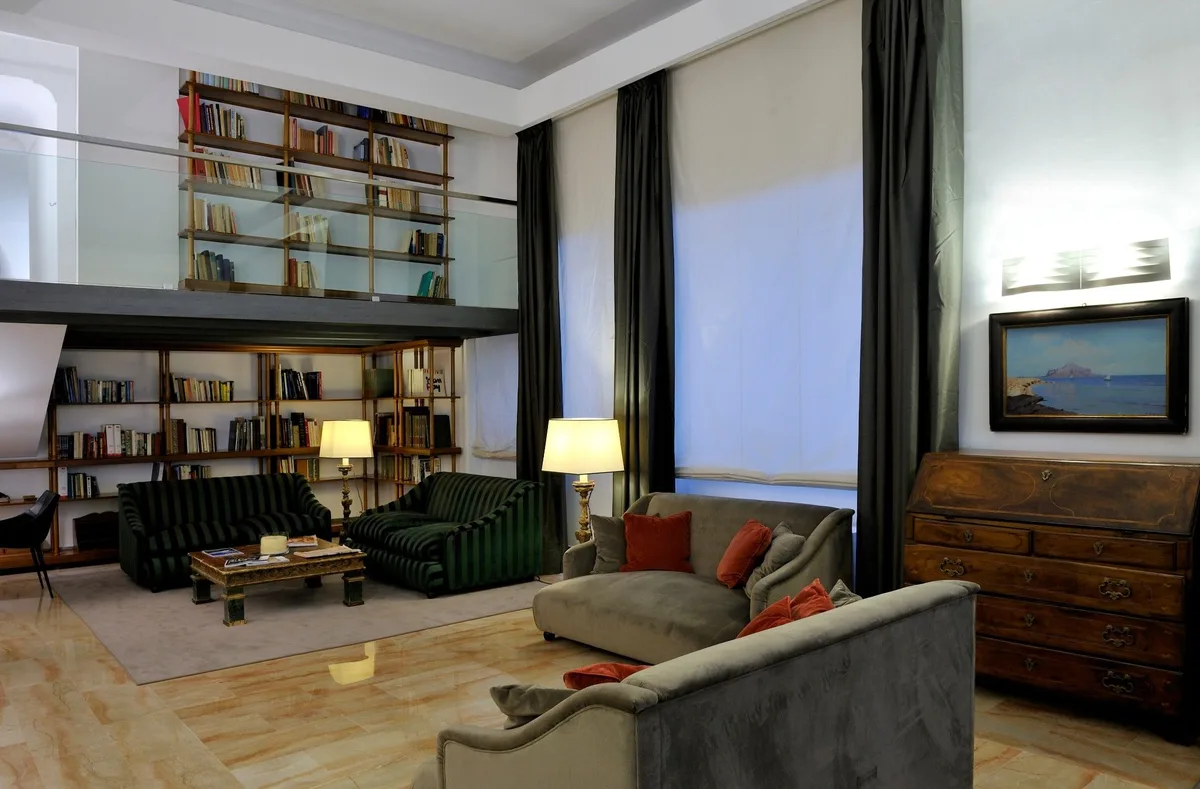 Elegante salotto con libreria a doppia altezza, divani, poltrone in velluto e cassettiera antica