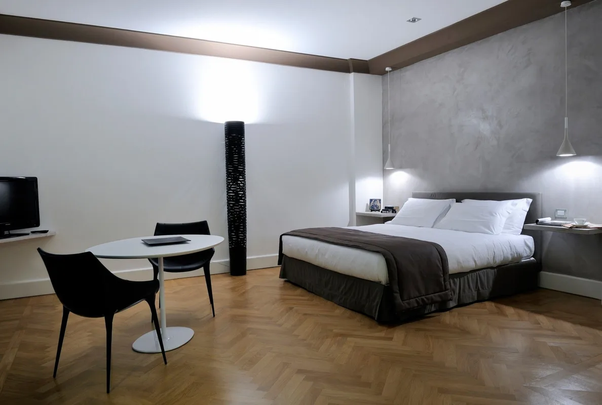 Ampia camera dallo stile minimalista con parete grigia, letto matrimoniale, tavolino e pavimento in parquet