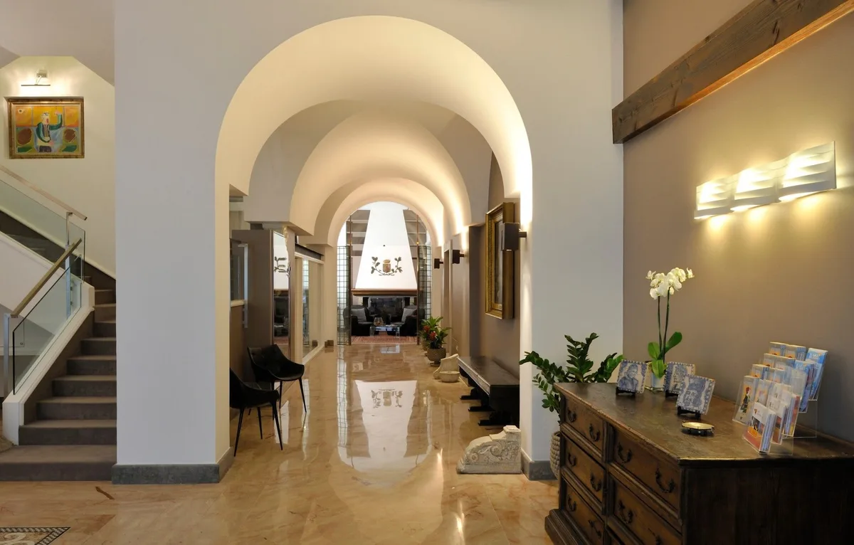 Hall dell'hotel con soffitti ad arco, scala, pavimento lucido in marmo e mobile antico con brochure