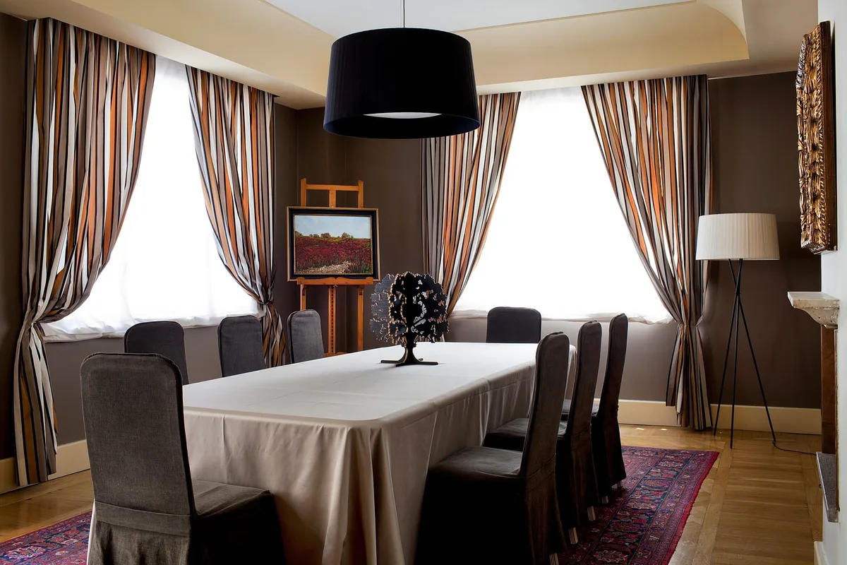Sala meeting con tavolo rettangolare, sedie con coprisedia grigie, tende a righe e opere d'arte
