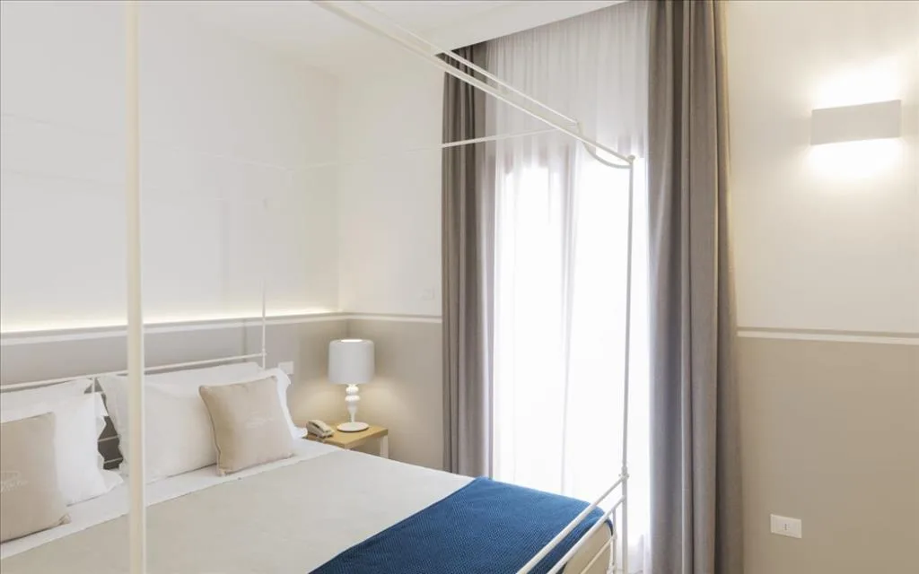 Camera con letto a baldacchino, plaid blu, comodino in legno e lampada da tavolo