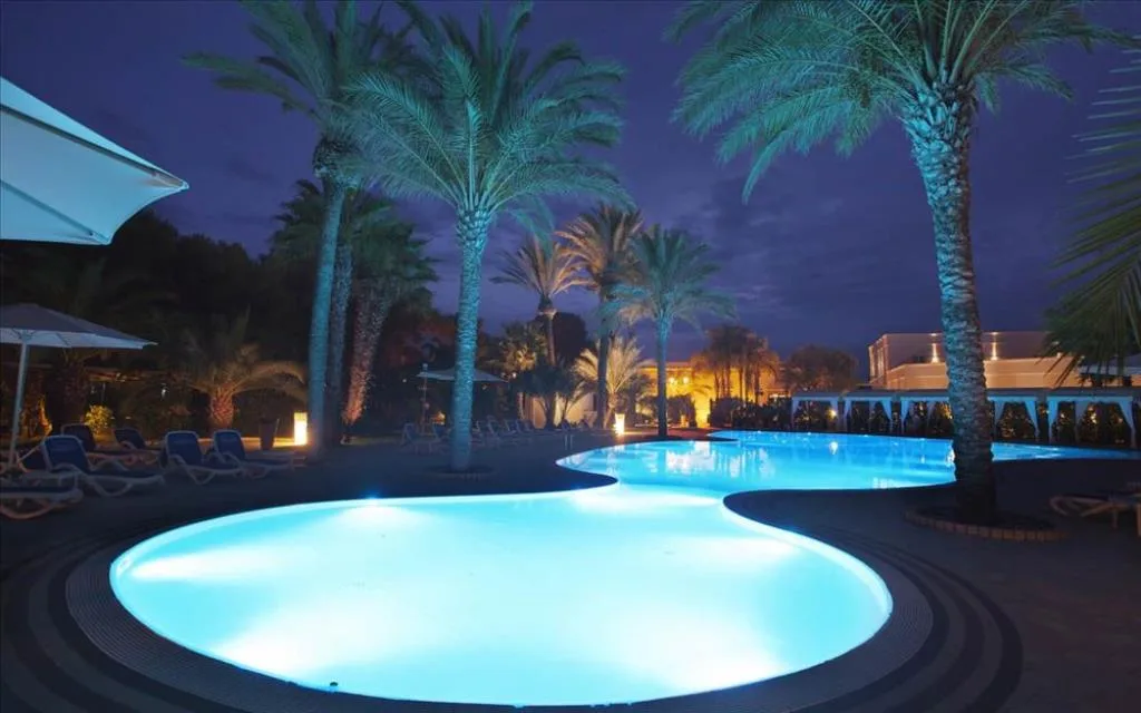 Piscina illuminata di sera con palme e lettini, atmosfera suggestiva notturna