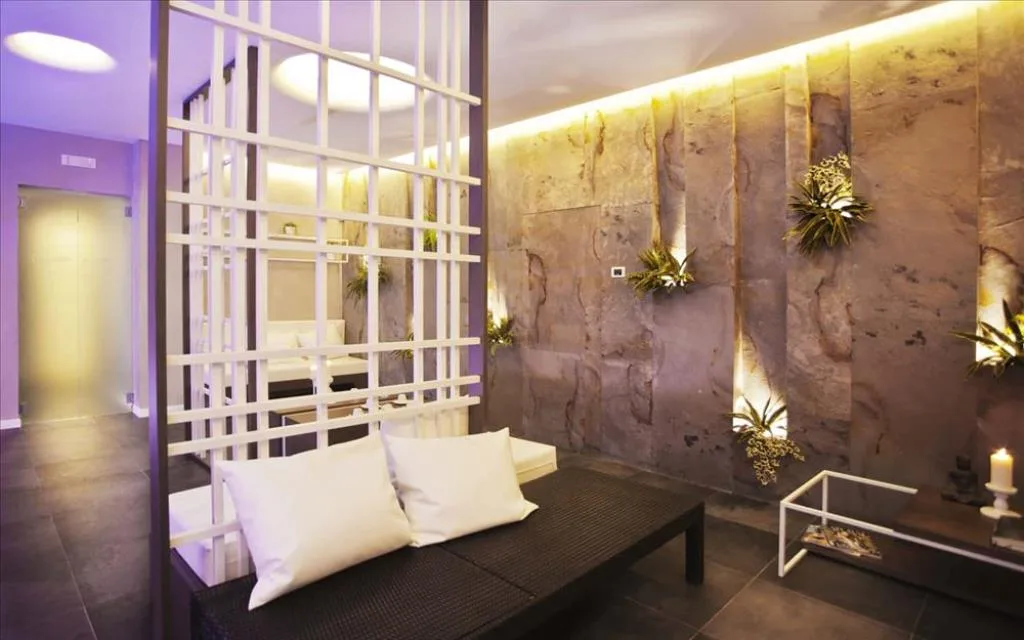 Area relax spa con divano, parete in pietra illuminata, piante e candela