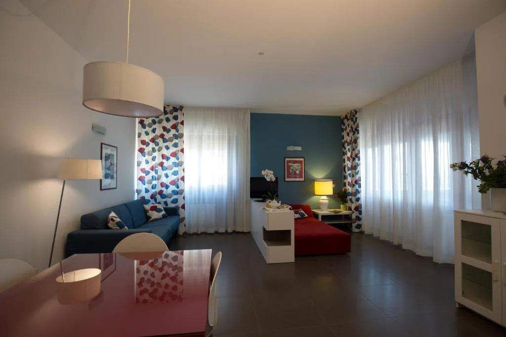 Ampio soggiorno con divano blu, chaise longue rossa, tende bianche e tavolo da pranzo