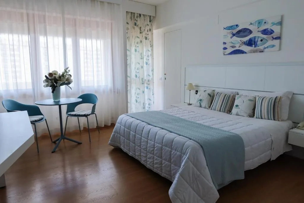 Camera luminosa con letto matrimoniale, tavolino con sedie azzurre e decorazioni a tema marino