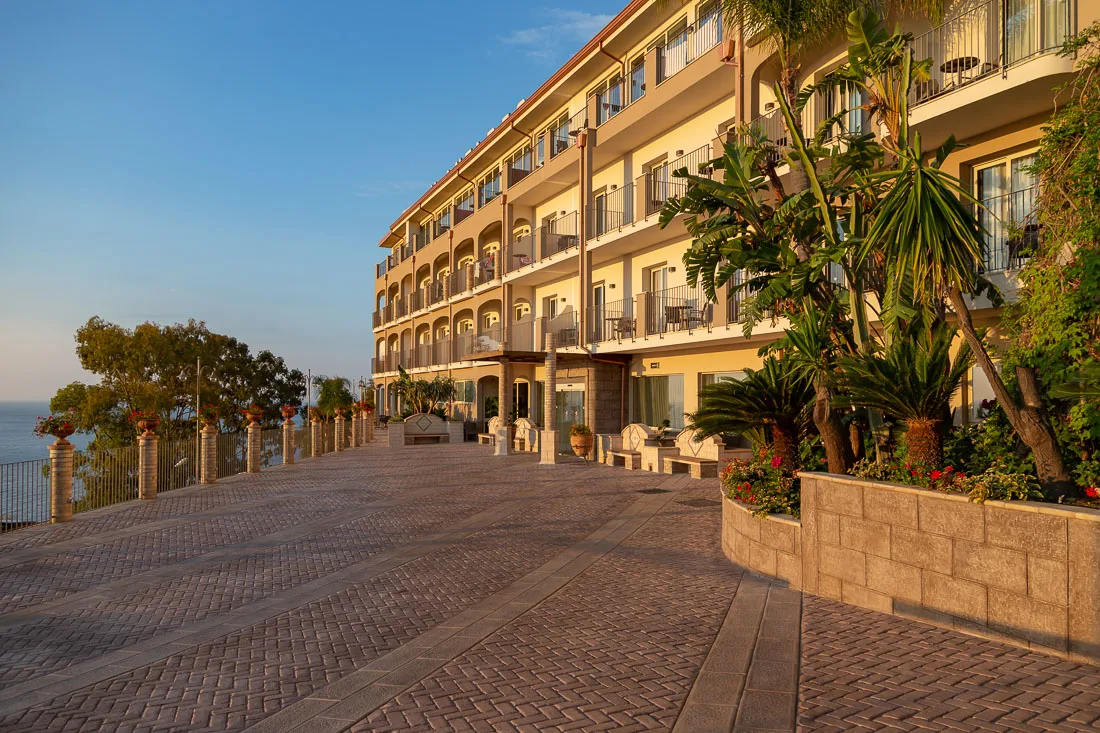 Ingresso dell'hotel con ampio vialetto pavimentato e palme al tramonto