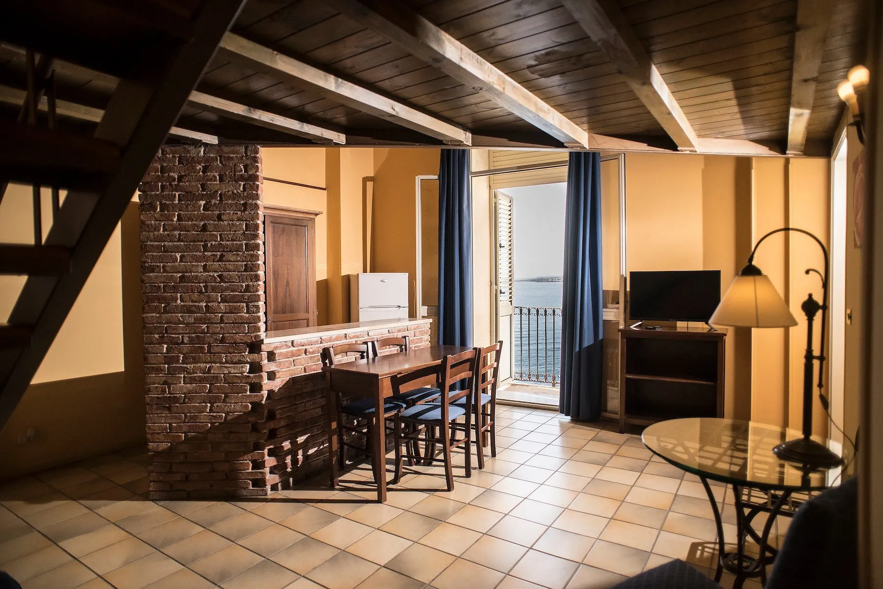 Soggiorno mansardato con travi in legno, parete in mattoni e balcone con vista mare
