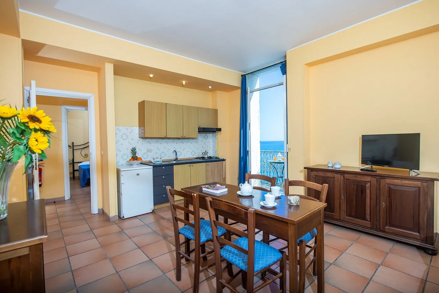 Soggiorno con angolo cottura, tavolo da pranzo e balcone con vista mare