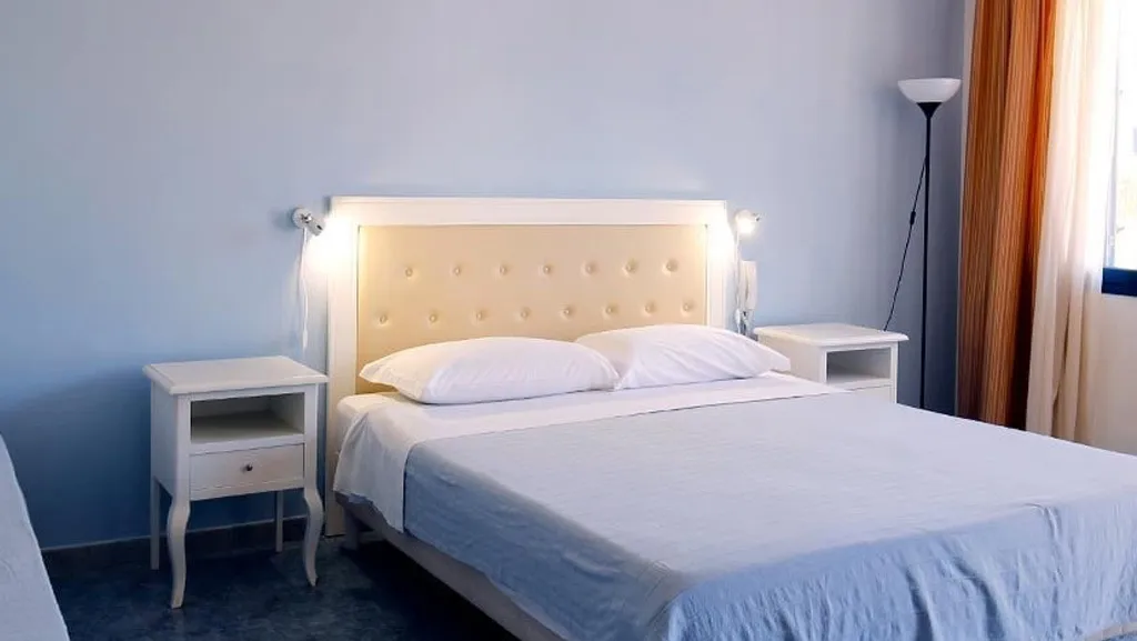 Camera luminosa con letto matrimoniale, comodini bianchi e pareti azzurre