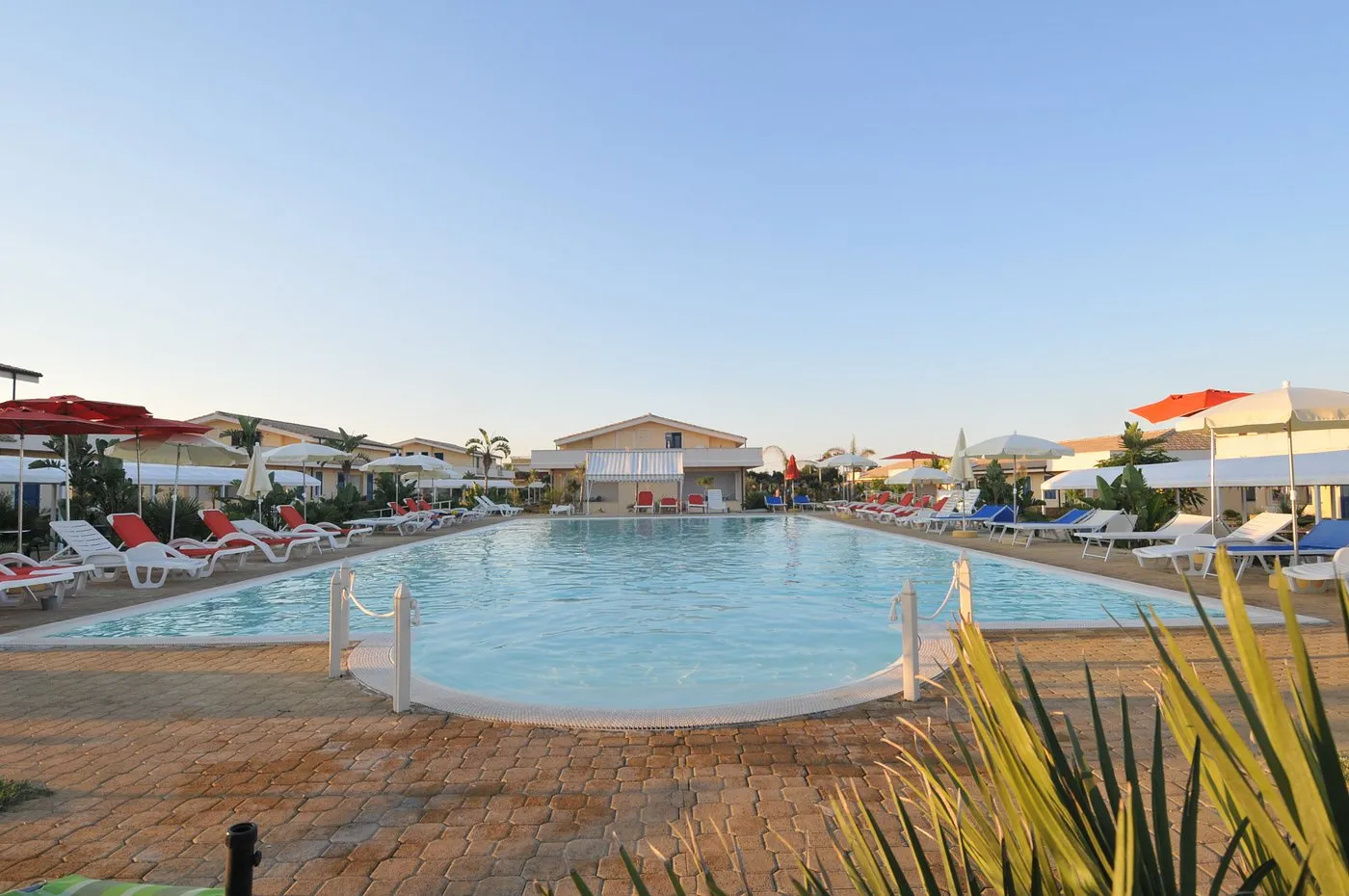 Grande piscina con lettini e ombrelloni colorati e villette sullo sfondo al tramonto