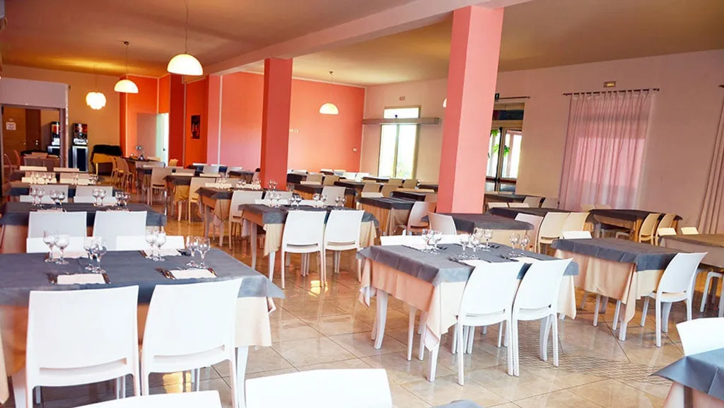Sala ristorante con tavoli apparecchiati, sedie bianche e pareti color corallo