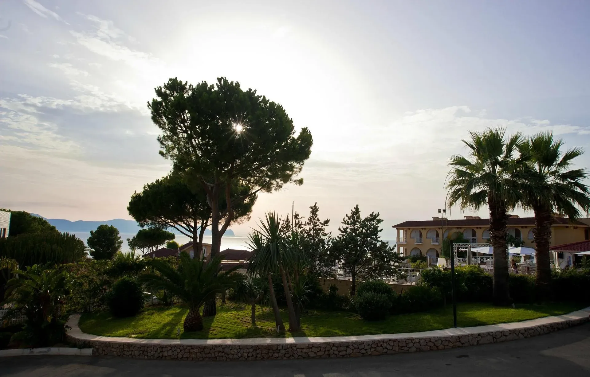 Giardino del resort con pini e palme al tramonto con vista sul mare
